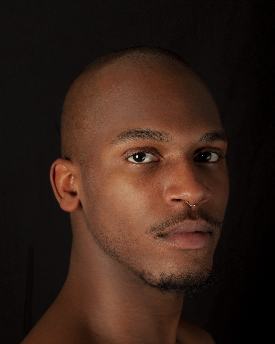 close portrait of man looking directly at camera against dark background