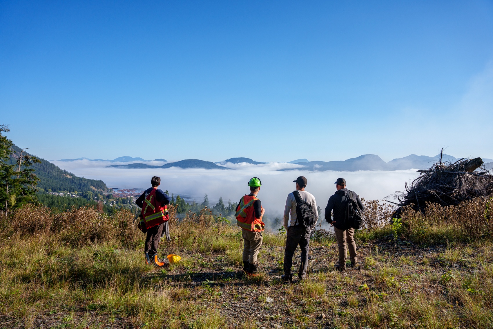 Four individuals survey a scene of a low cloud inversion with rounded mountain peaks poking through.