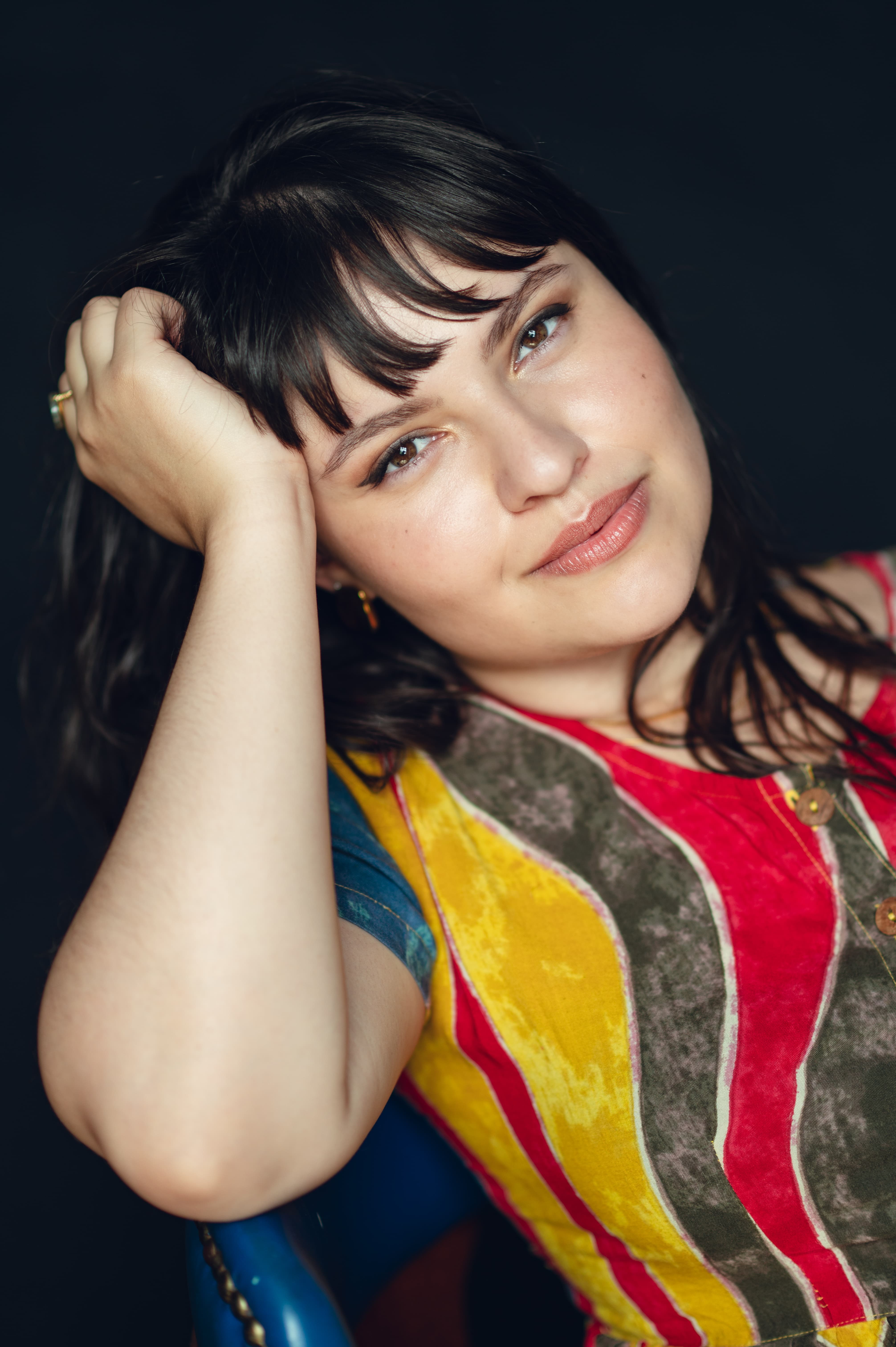 Woman wearing colourful shirt holding head up with hand looking directly at camera