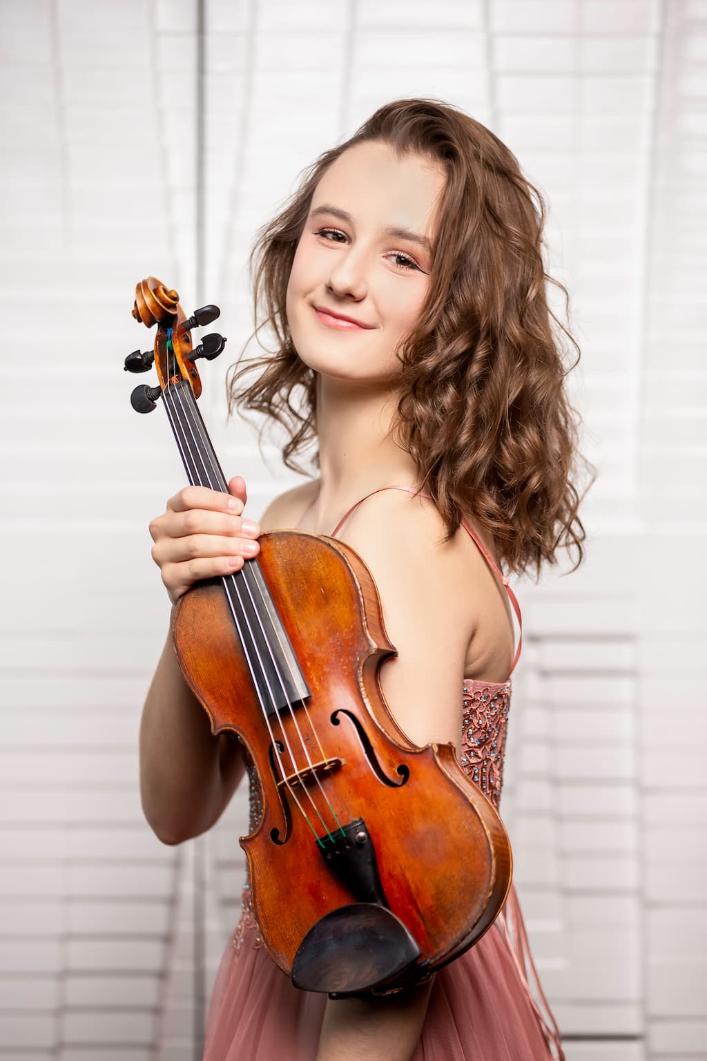 Anna Stube is holding a violin and looking towards the camera smiling