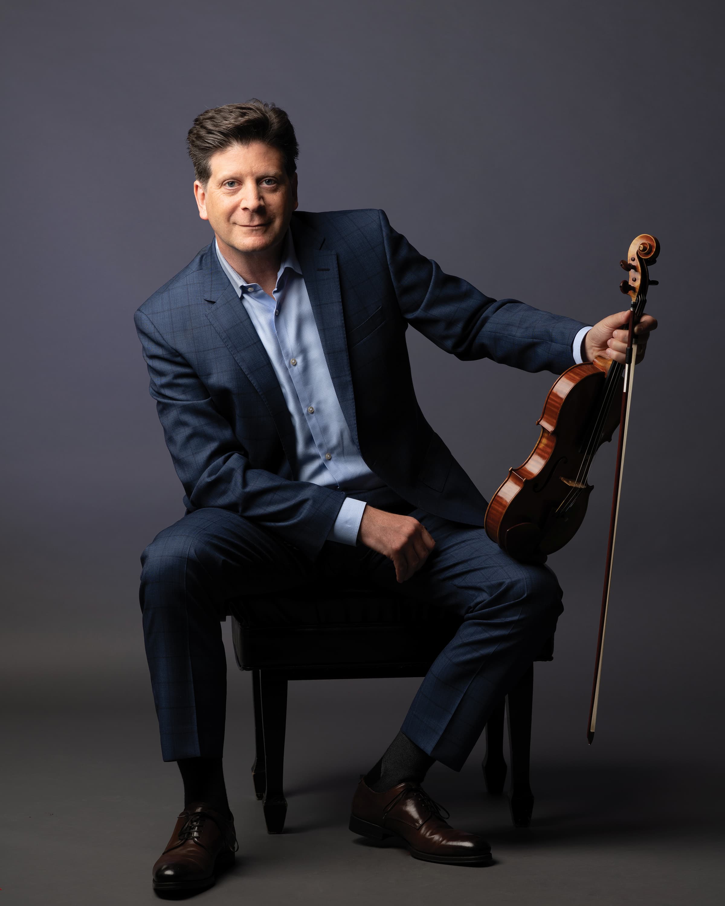 Barry Shiffman is seated on a chair with a violin resting on his knee.