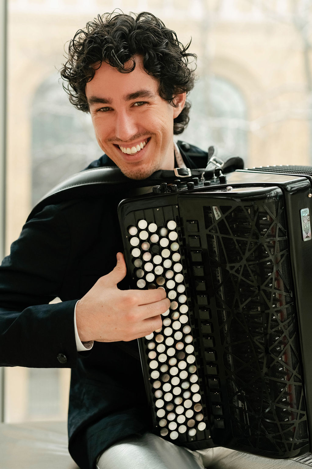 Michael Bridge is playing a black accordion and smiling at the camera Michael Bridge is playing a black accordion and smiling at the camera