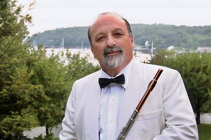 Thomas Wolf is wearing a white jacket, black bowtie, and holding a flute