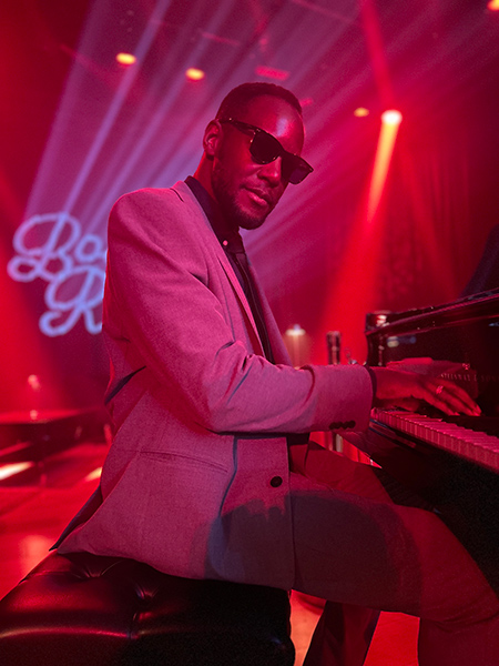 Timothonius wearing sunglasses playing the piano in dark club
