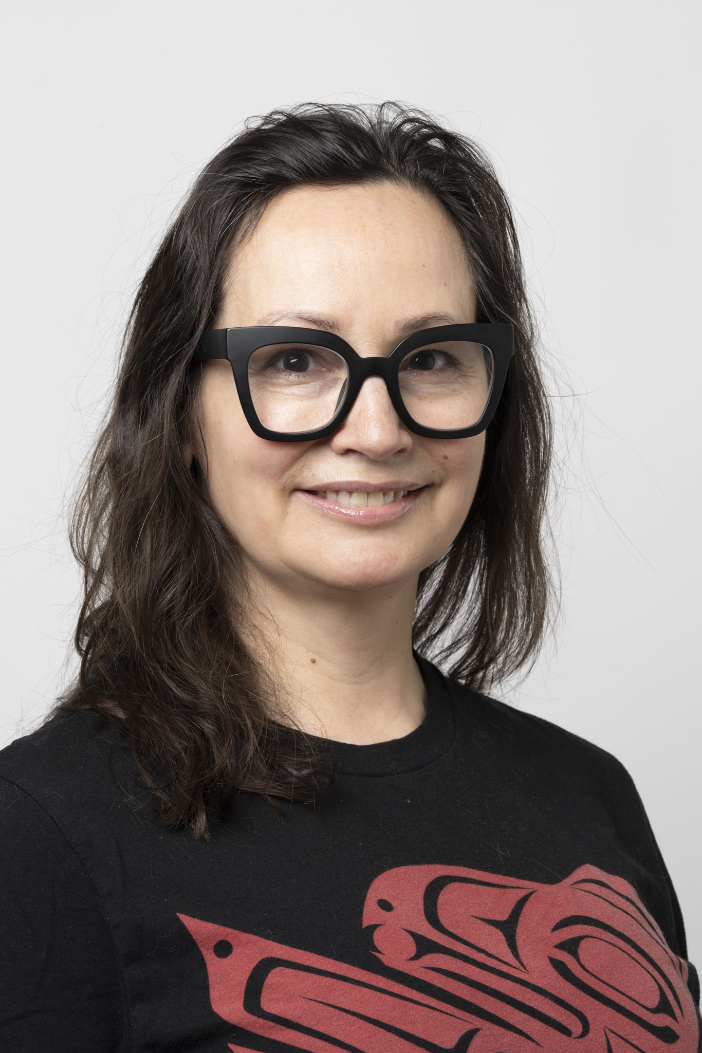 Woman with long hair and thick black glasses smiling directly at camera