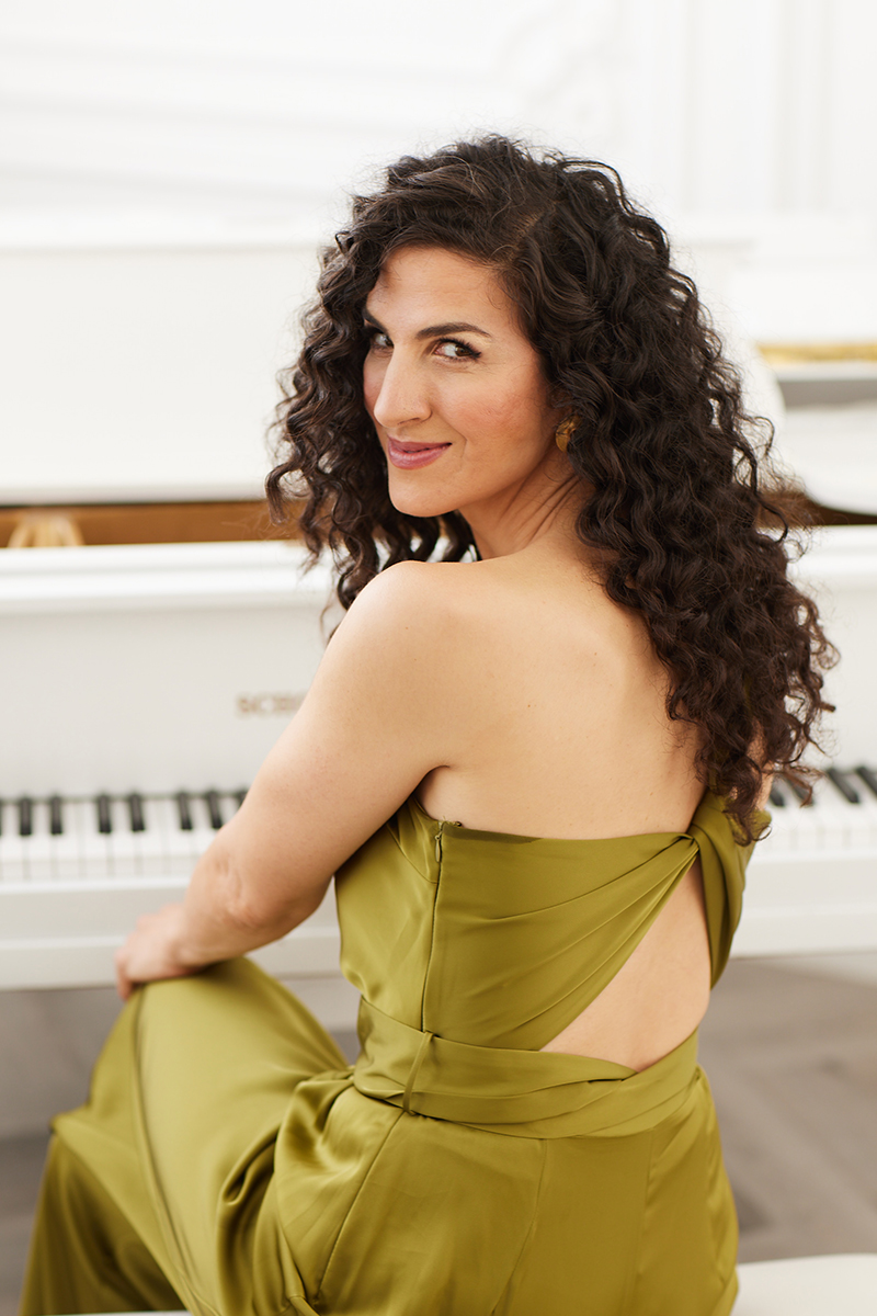 smiling woman seating facing back with long dark hair wearing green dress 