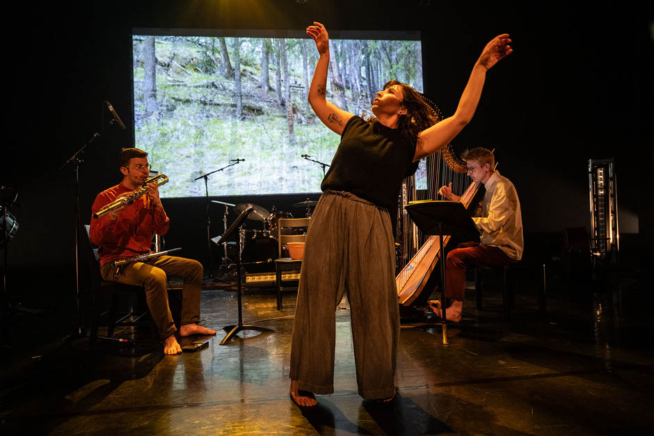 A woman dances on stage between a flute player and a harpist