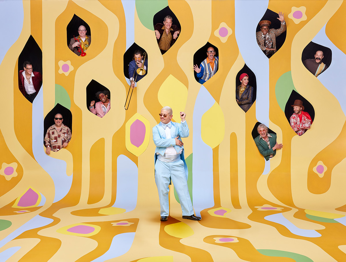 Pink Martini music group take the pose in front of a funky backdrop yellow and blue 