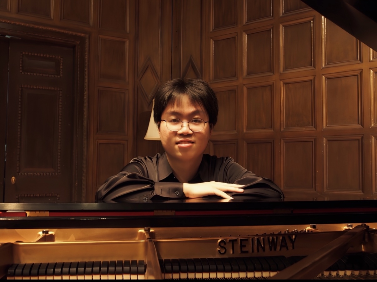 Man leaning over piano in black shirt looking at camera