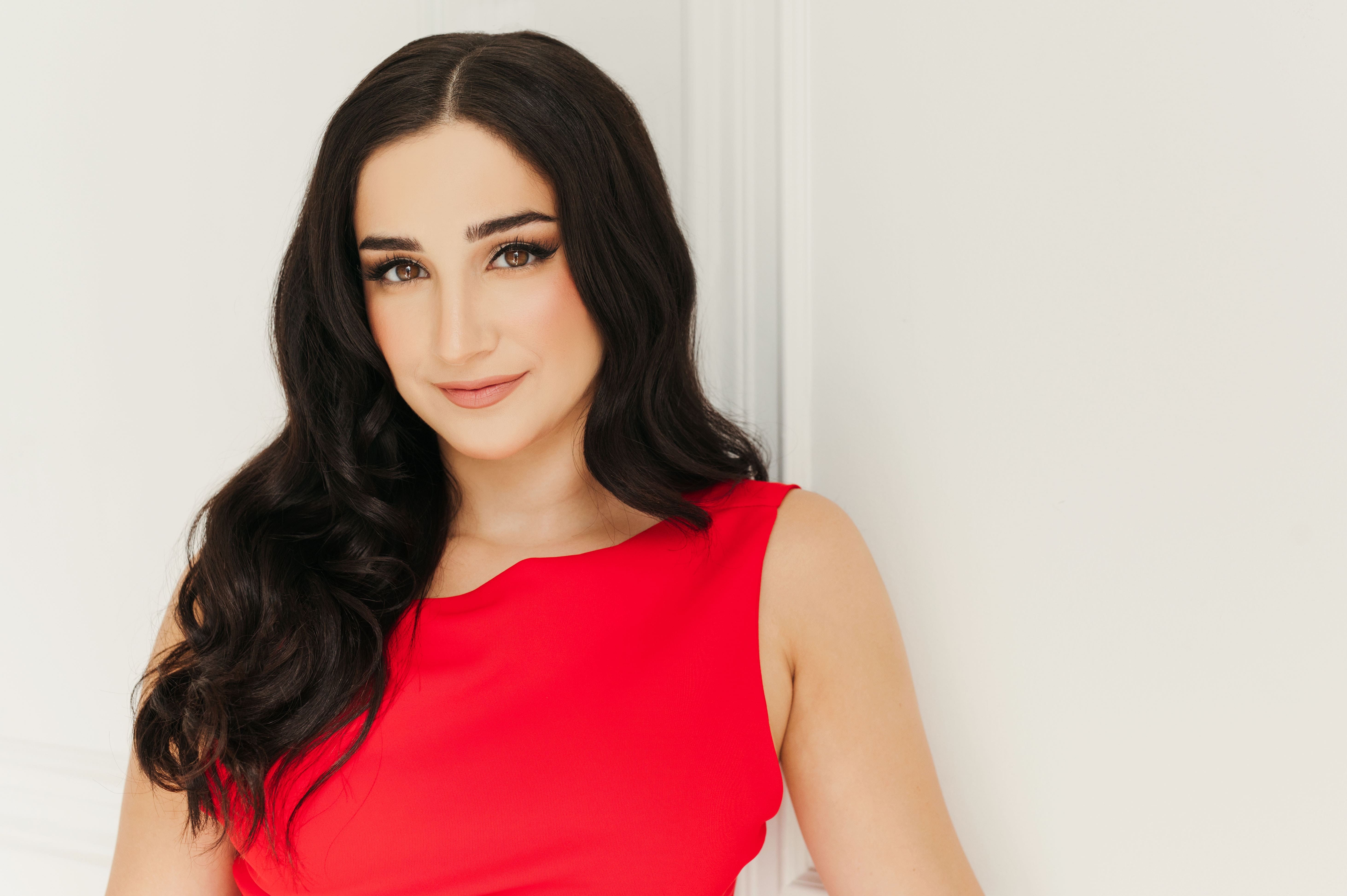 Woman with long black hair covering shoulders smiling lightly at camera in bright red dress