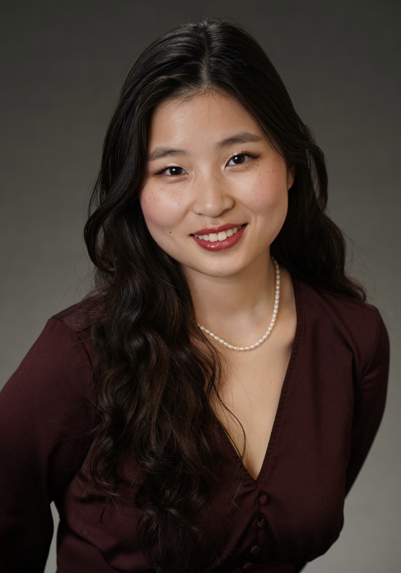 Woman in black shirt and pearl necklace looking directly at the camera