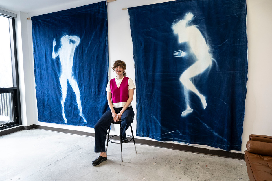 An artist is sitting in front of two large tapestries