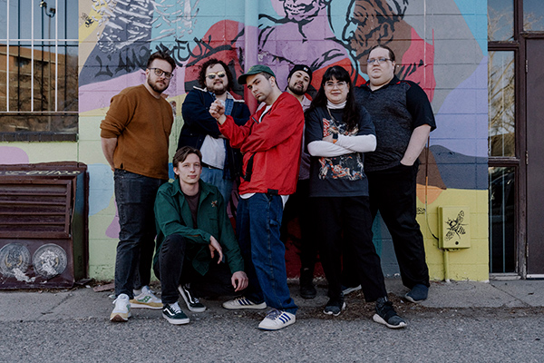 Midnight channel collective standing against a graffitied wall. 