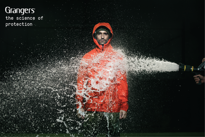 A man in a red jacket is getting blasted by water from a fire hose.