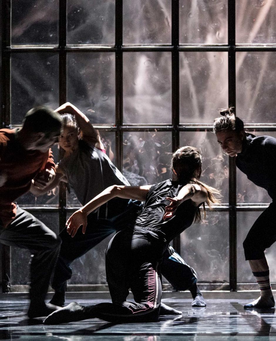 Four dancers performing on a dark stage.