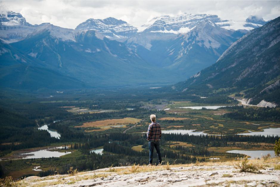 Joel Ivany stands atop a mountain overlooking a mountain range.