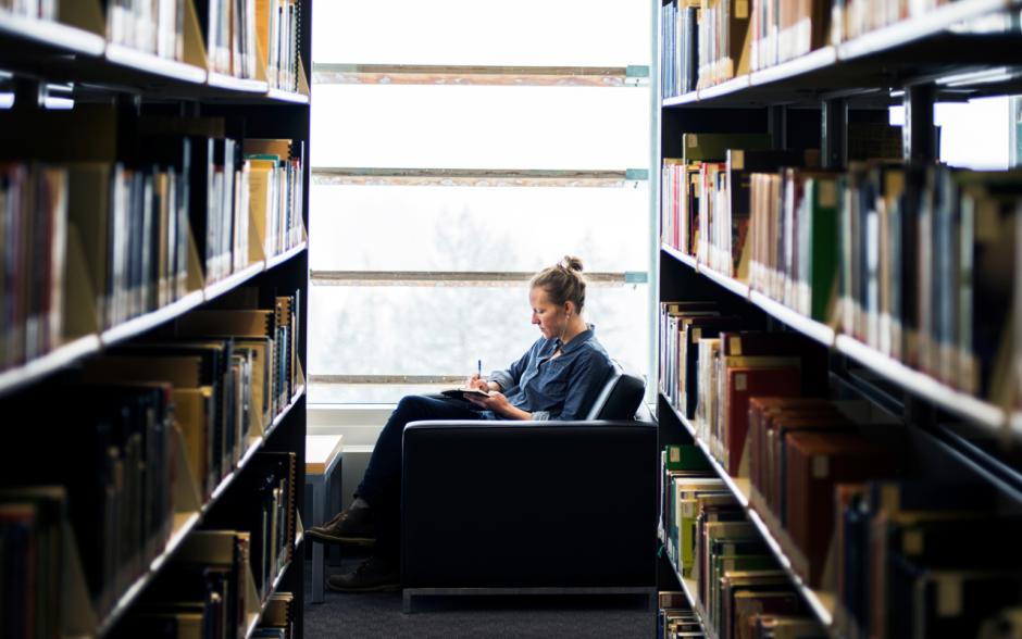 Kate Harris writing next to a window in the library. 