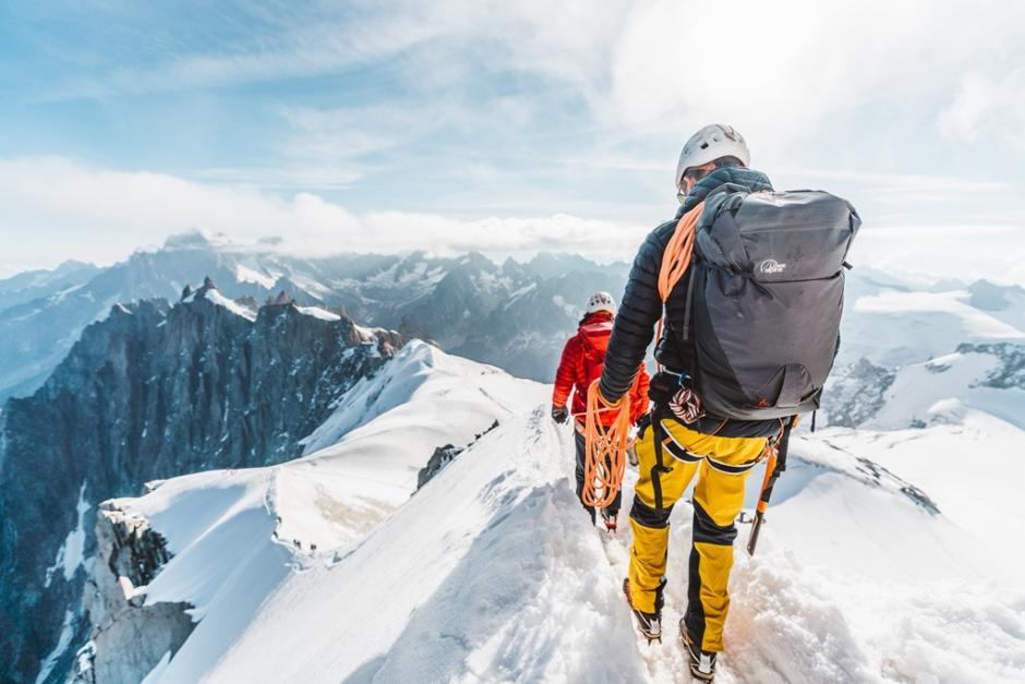 Mountaineers walk on high snowy ridge.