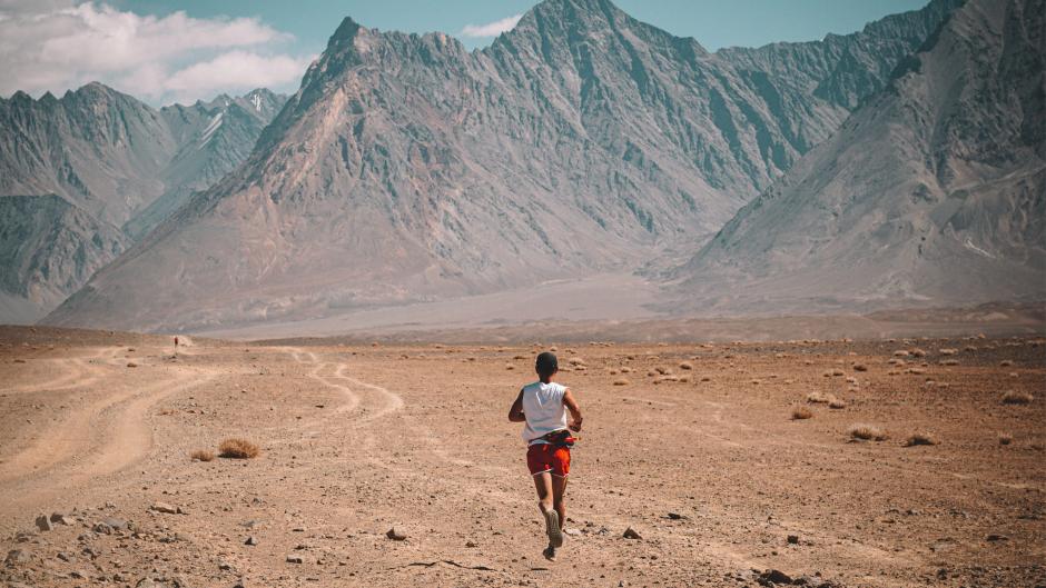 Athlete runs across sand and dirt in a dry mountain range. 