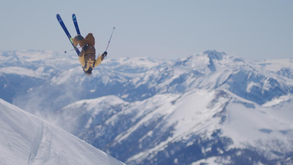 Skiier performs a backflip with a mountain range in the background.