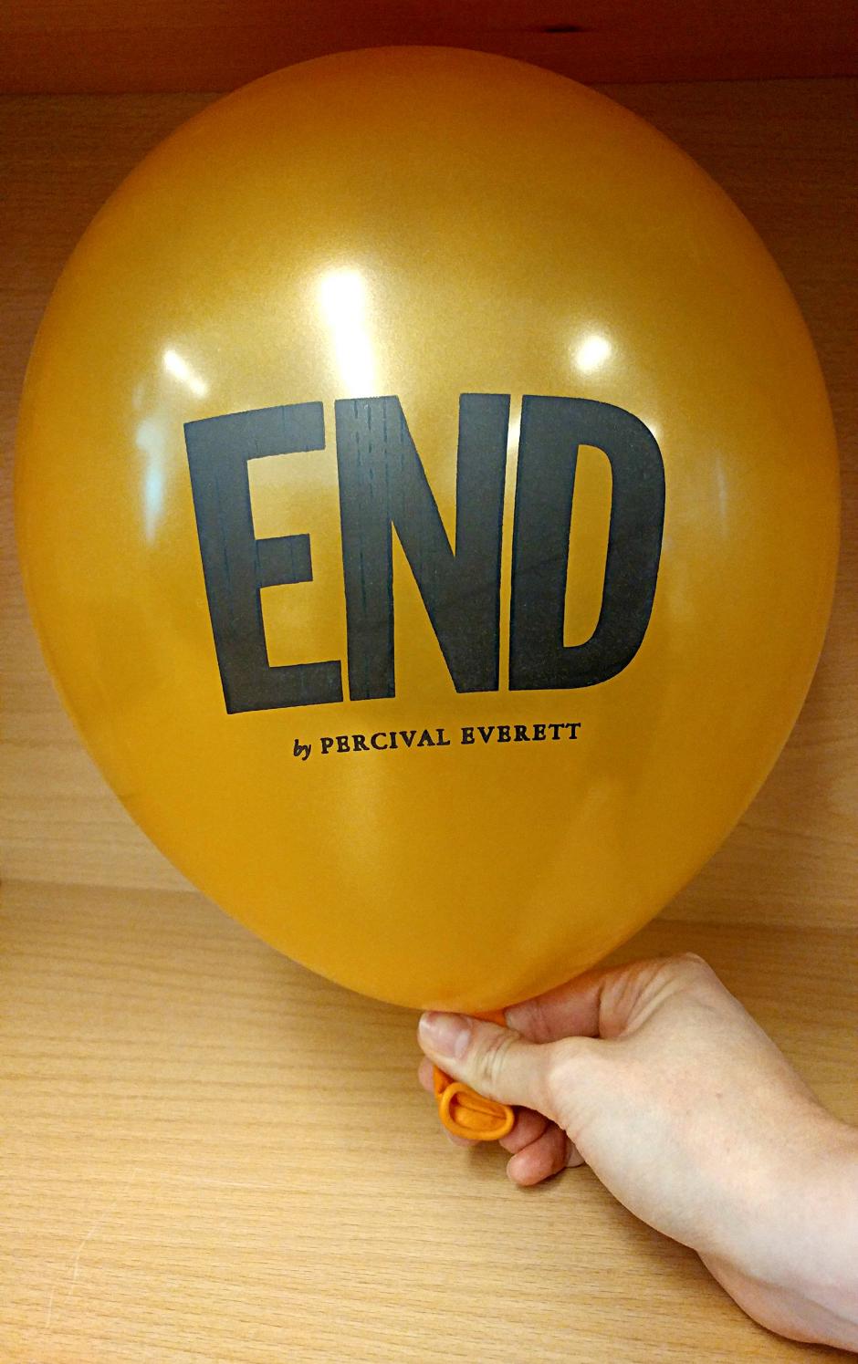 A golden balloon inflated with the text, "End by Percival Everett" printed on it. 