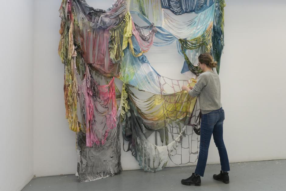 An artist manipulates multi-coloured fabric draped from a wall.