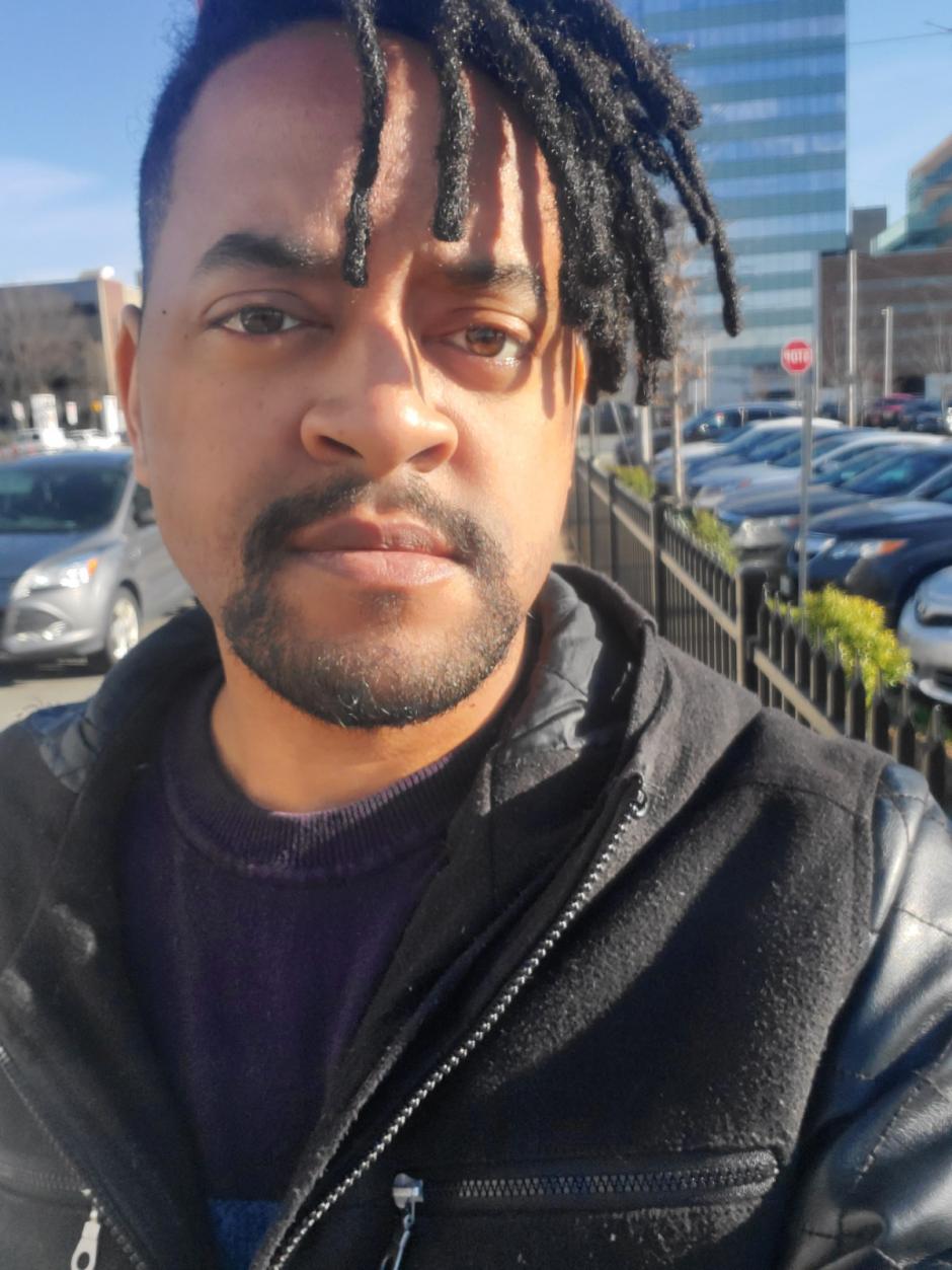 Damon Reaves wears a leather jacket over a T-shirt and is sporting a goatee and dreads.