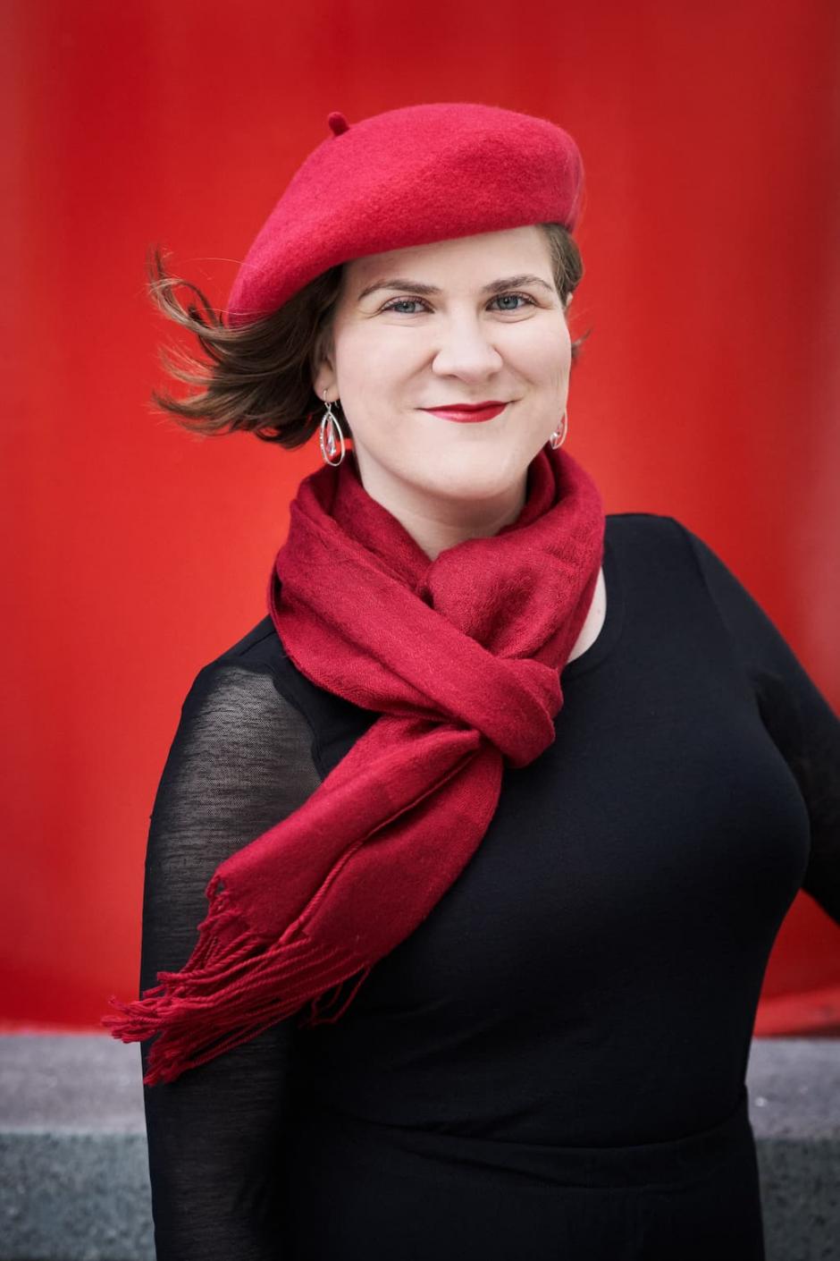 Ema Nikolovska is wearing a black top, red scarf and red beret, and smiling at the camera