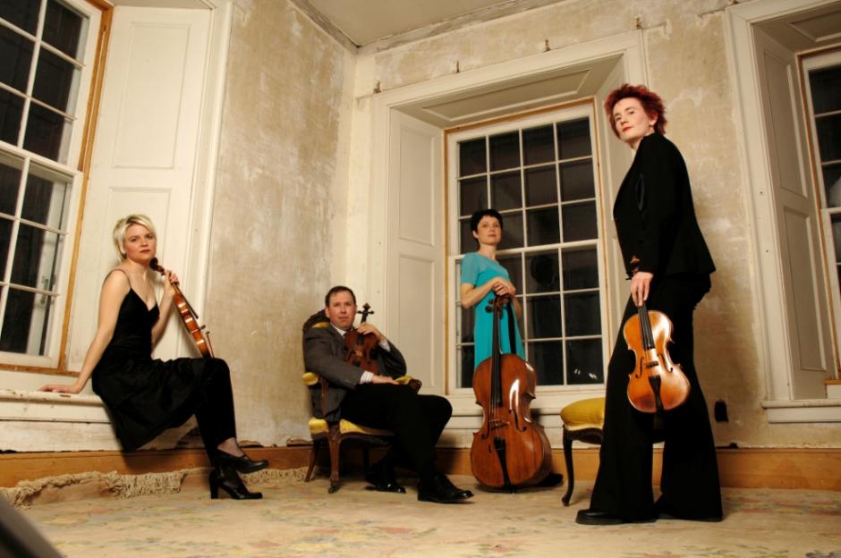 The Eybler Quartet, a Banff Centre Faculty Quartet, poses in front of a series of windows set into an inside corner of an old stone building.