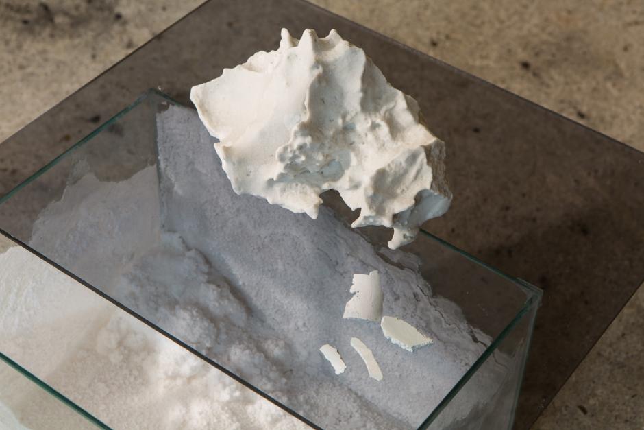 A many edged white stone sits atop a 3D glass rectangle with white sand inside the rectangle.