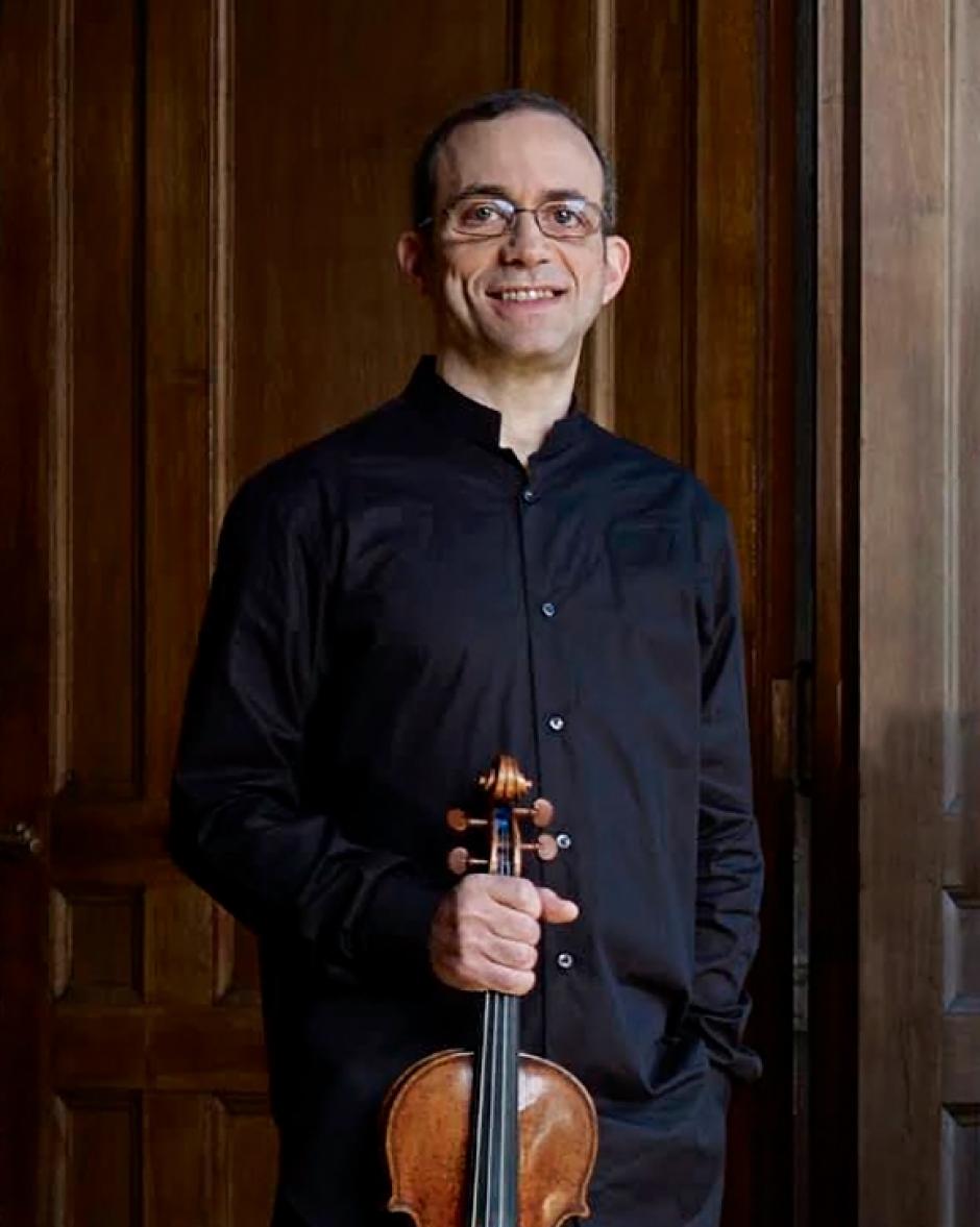 Mark Steinberg stands holding violin and smiling towards camera