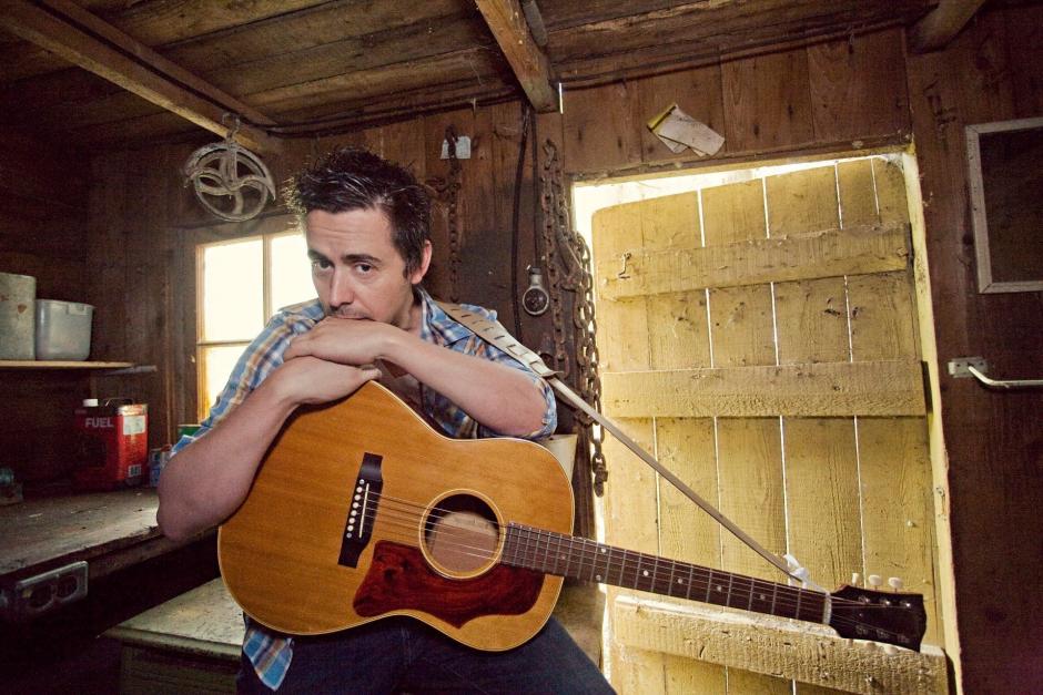 Danny Michel is seated with both arms resting on the guitar on his lap