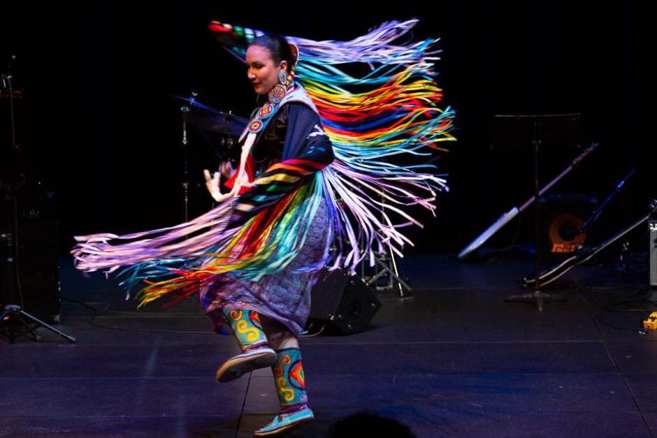 Indigenous woman in colourful ribbon regalia dances on stage