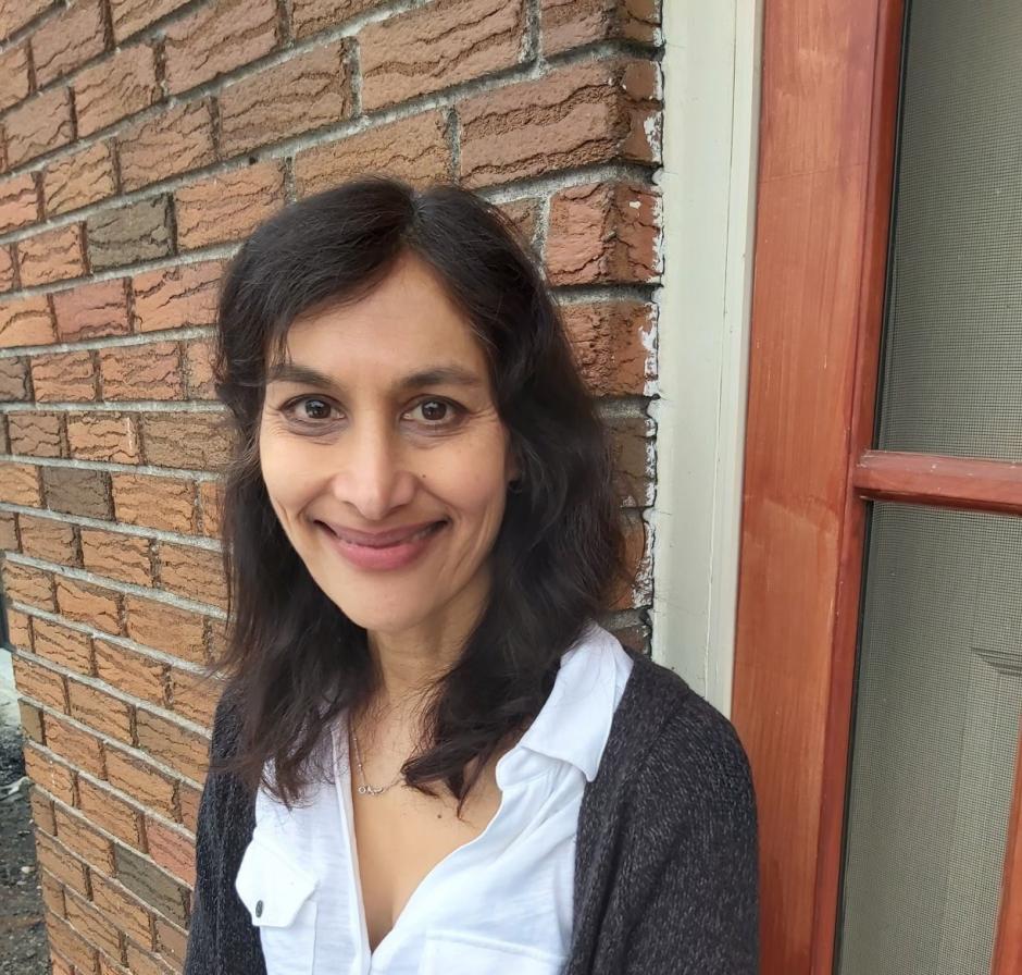 Photo of program faculty, Anita Anand, smiling into the camera, with a brick wall backdrop