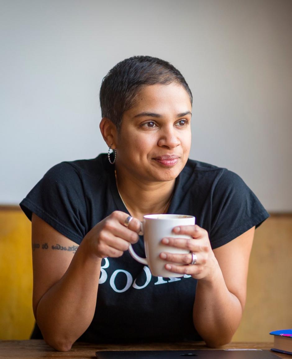 Photo of program faculty, Tanya Boteju, relaxed and smiling, leaning forward with coffee mug held in both hands