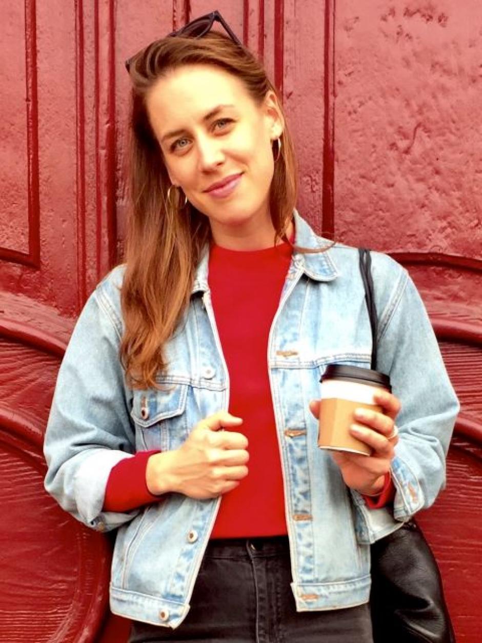 Anika Johnson stands in front of red wall holding a coffee cup and smiling
