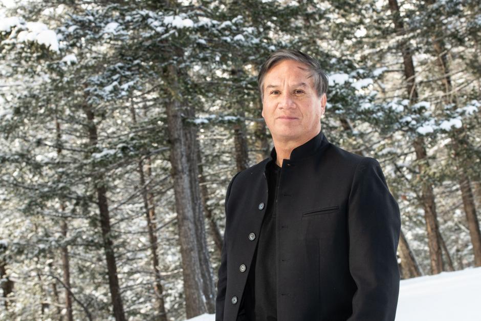 Alejandro Ronceria stands in front of a stand of snowy pine trees