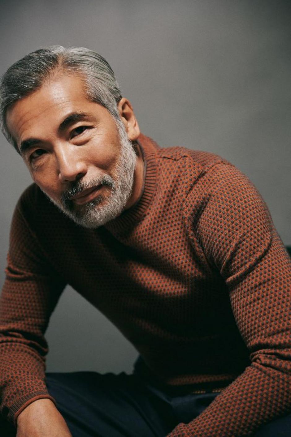 Hiro Kanagawa is wearing a rust coloured sweater. He is seated, and leaning forward, looking into the camera.