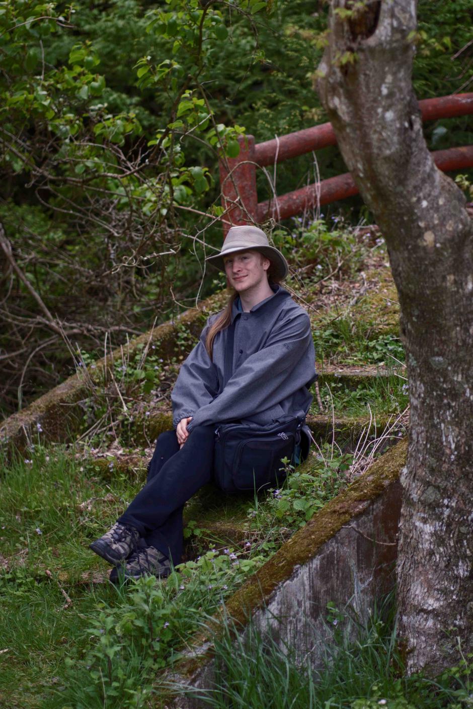 Cole Dorchester sitting outside on stairs overgrown with grass in a forest