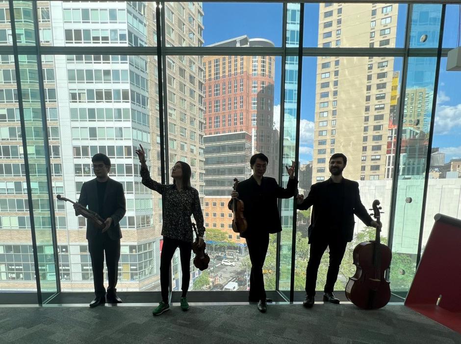 Members of Napoletano Quartet backlit in front of a large window showing a city scape behind them