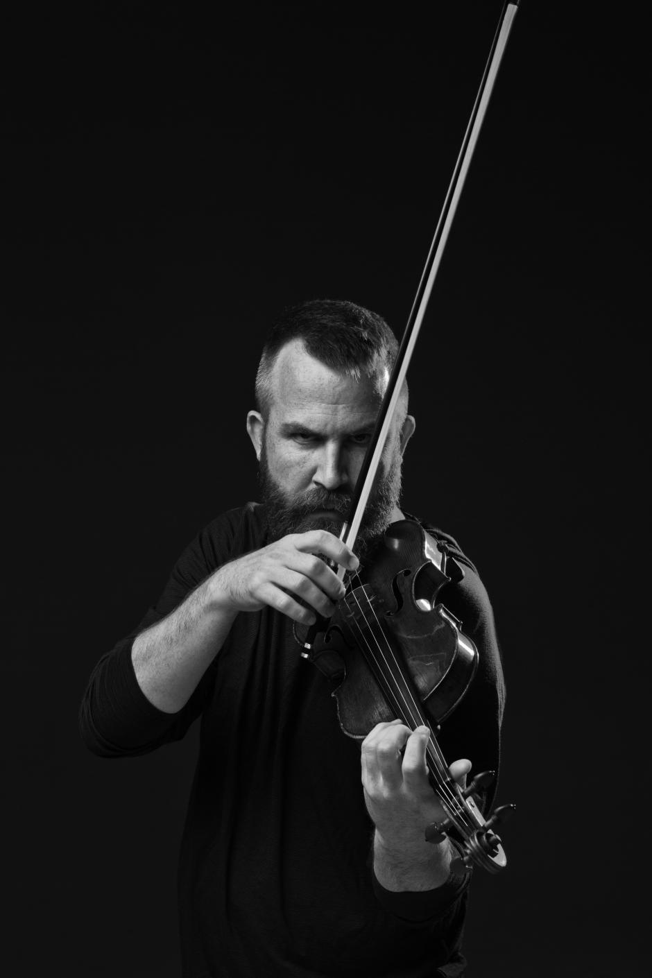Black and white photo of man looking at camera while holding a violin