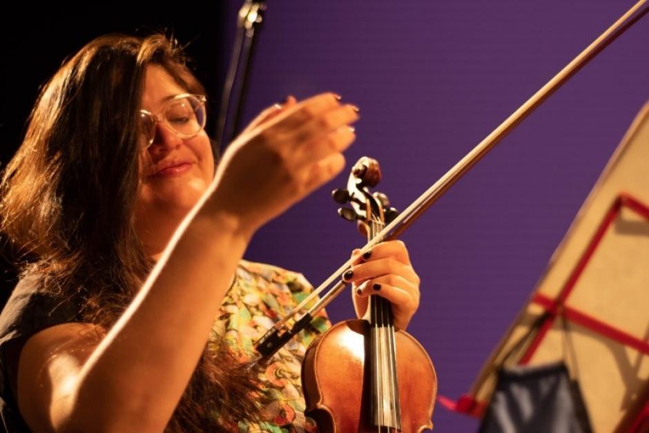 Alejandra pictured here with a purple background holding a violin. 