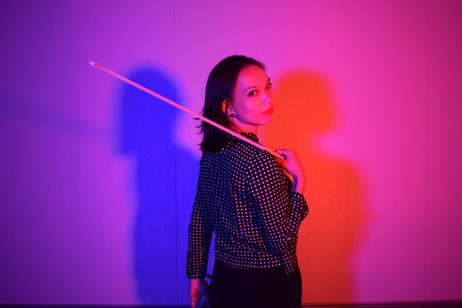 Teagan stands in front of blue and red light with a violin bow.