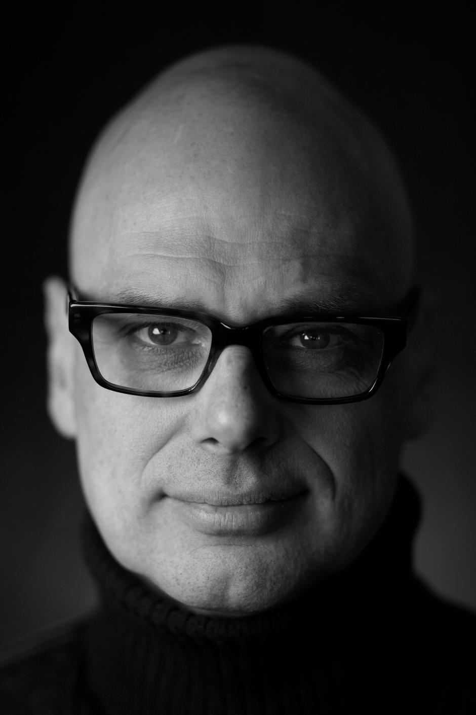 Multi-media designer, Hugh Conacher, wears glasses in a black and white photo