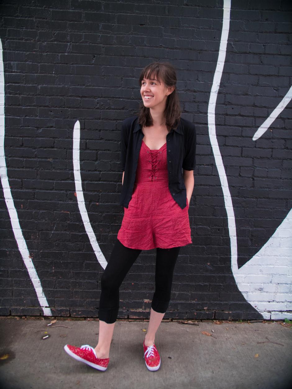 Stephanie stands with her hands in the pockets of her red and white jumper agains a black and white brick wall. 