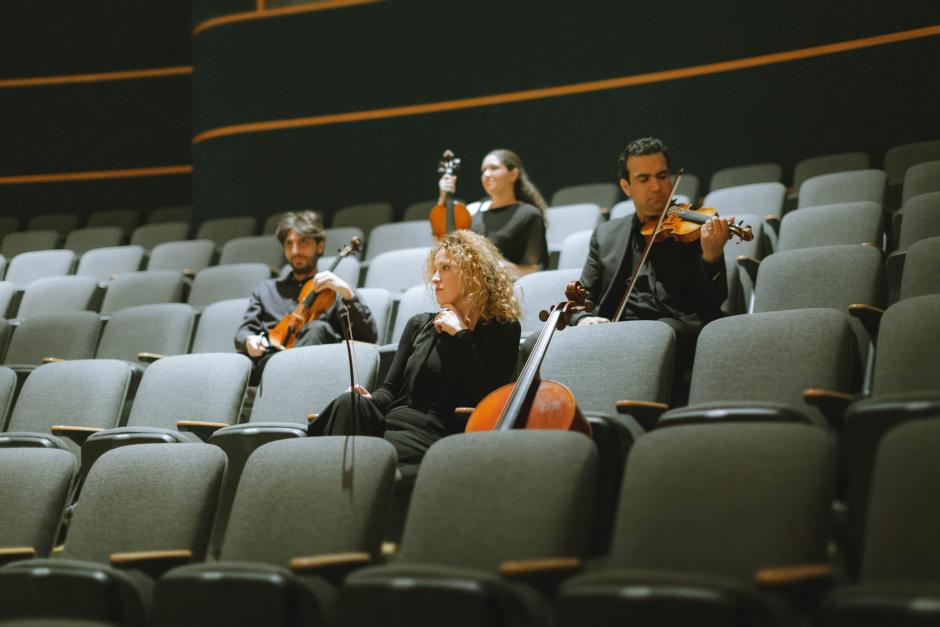 The members of the Vaughan String Quartet sit in the audience seats of a theatre holding their instruments