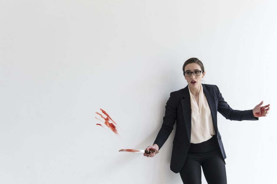 A woman stands surprised against a white background with blood on the knife and wall