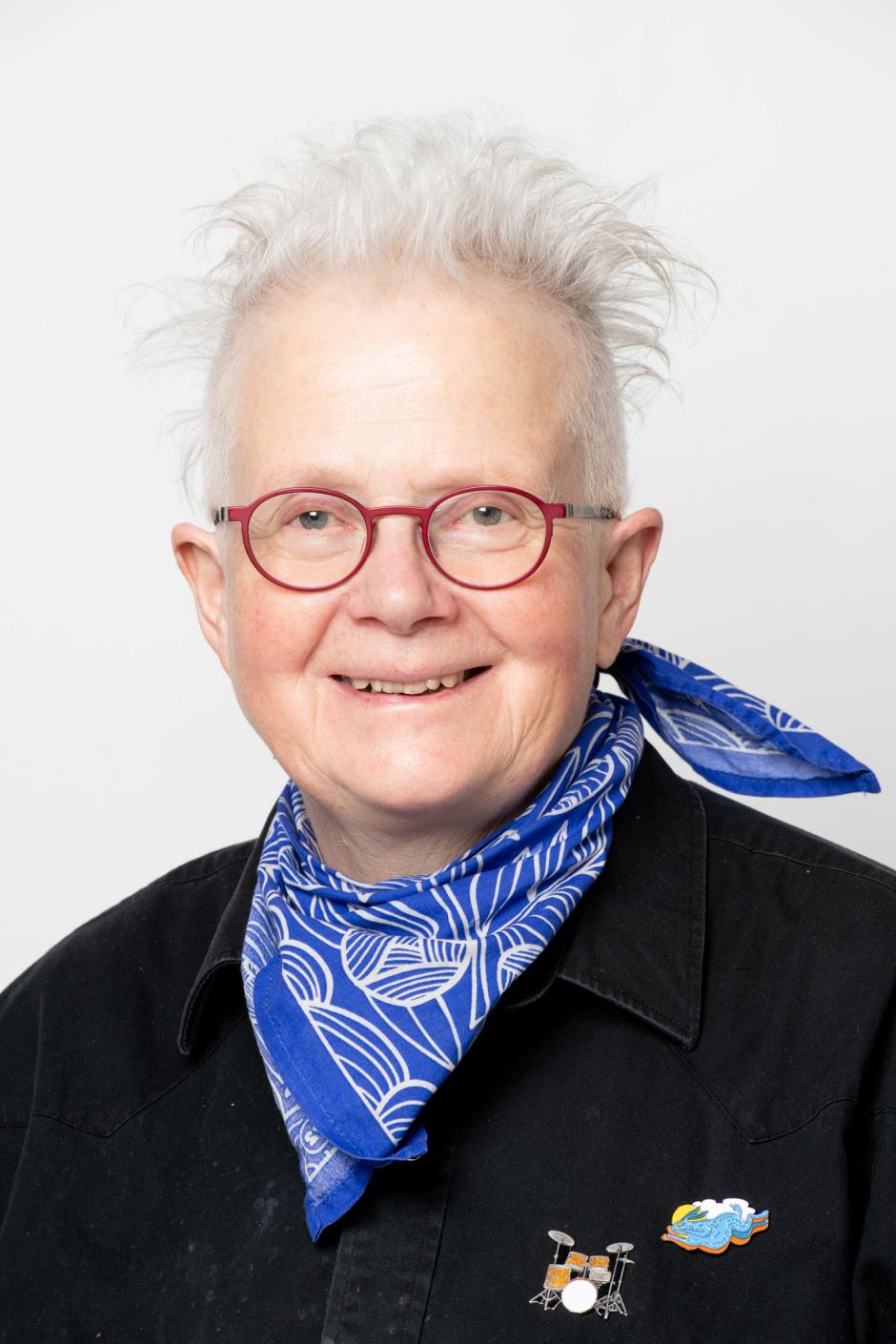 Rita McKeough smiles at the camera wearing red glasses and a blue scarf