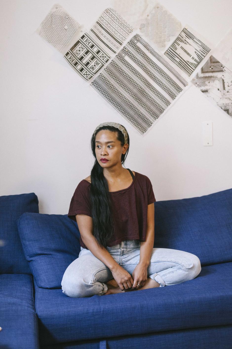 Photo of program faculty, Stephanie Comilang, sitting cross-legged on couch looking to her right