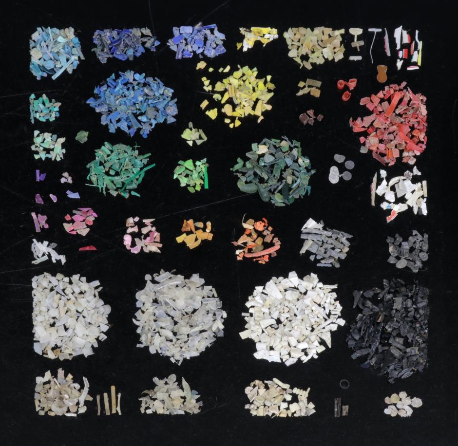 Photograph of various pieces of micro- and macro- plastic pollution from beach samples are spread out evenly over a smooth semi reflective surface
